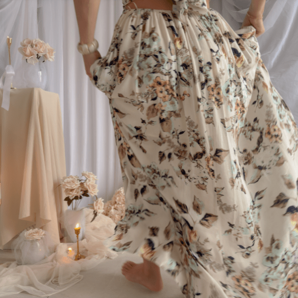 New arrival from the Coastal Romance Collection featuring a romantic floral halter maxi dress with an open back, flowy silhouette, and soft neutral coastal tones styled in an elevated feminine editorial setting.