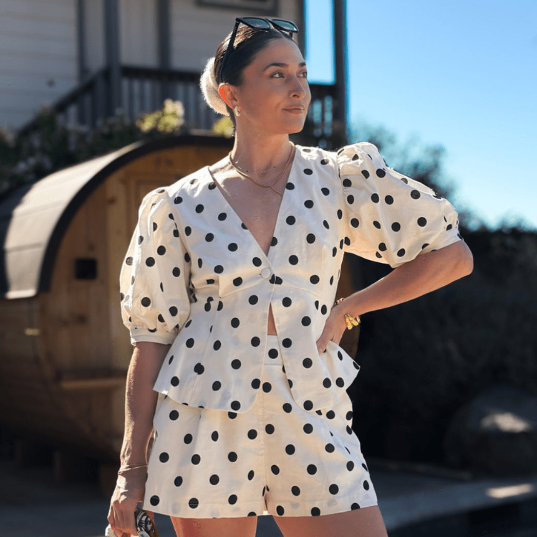 Woman wearing an ivory and black polka dot puff sleeve top and matching shorts from the Soft Heritage Romance fall collection by Blooming Daily.
