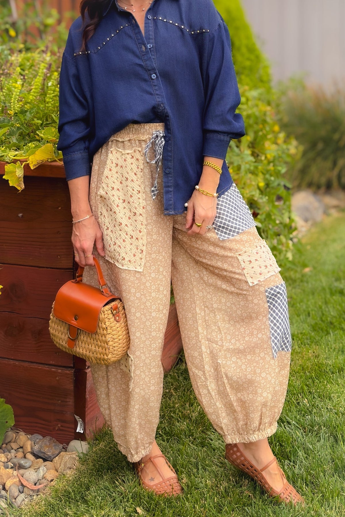 Woman wearing beige floral patchwork balloon pants with a cream wooden toggle cardigan, woven handbag and tan flats for a soft transitional outfit.