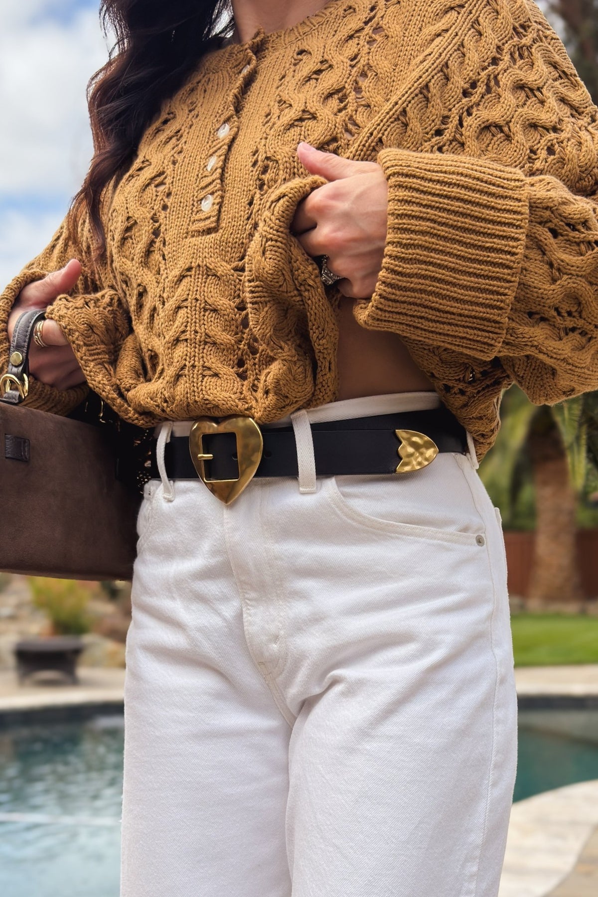 Black genuine leather statement belt with gold heart buckle styled with high-waisted white denim and textured knit sweater.