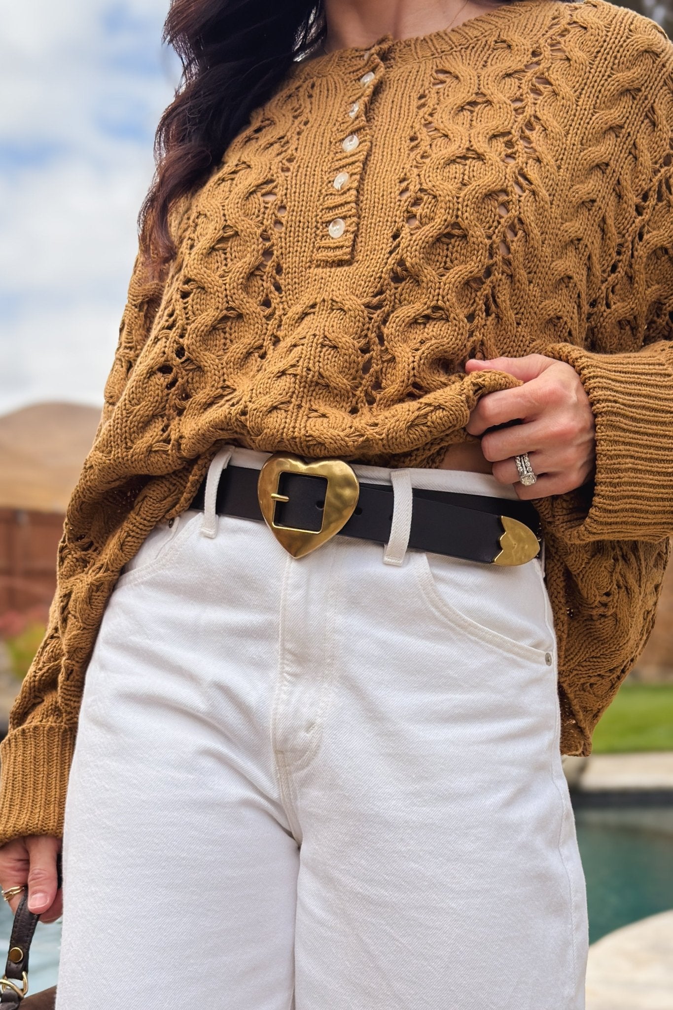 Black genuine leather heart buckle belt with oversized gold heart hardware styled with white jeans and a brown cable knit sweater.