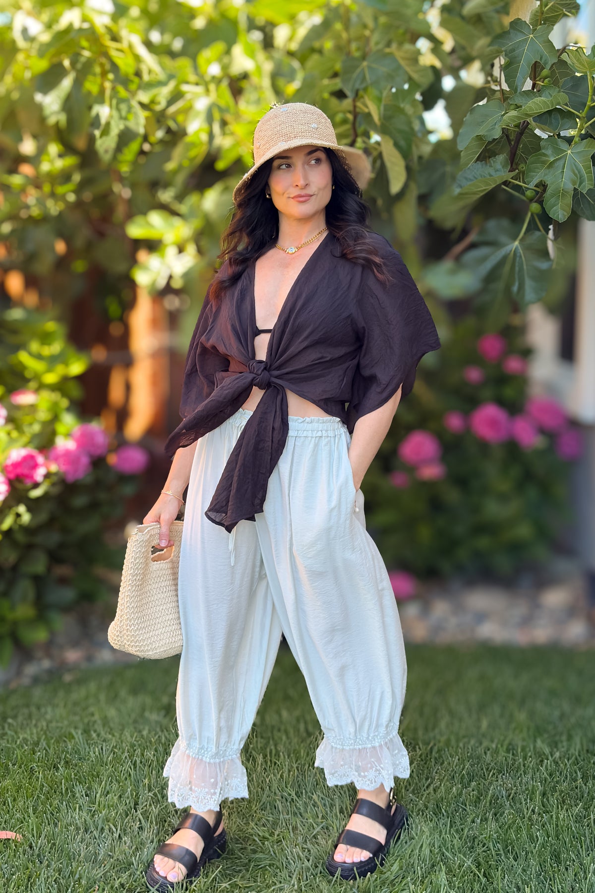 Black tie front kimono cover up top styled with cream lace hem pants, woven handbag, and straw hat for a feminine summer outfit.