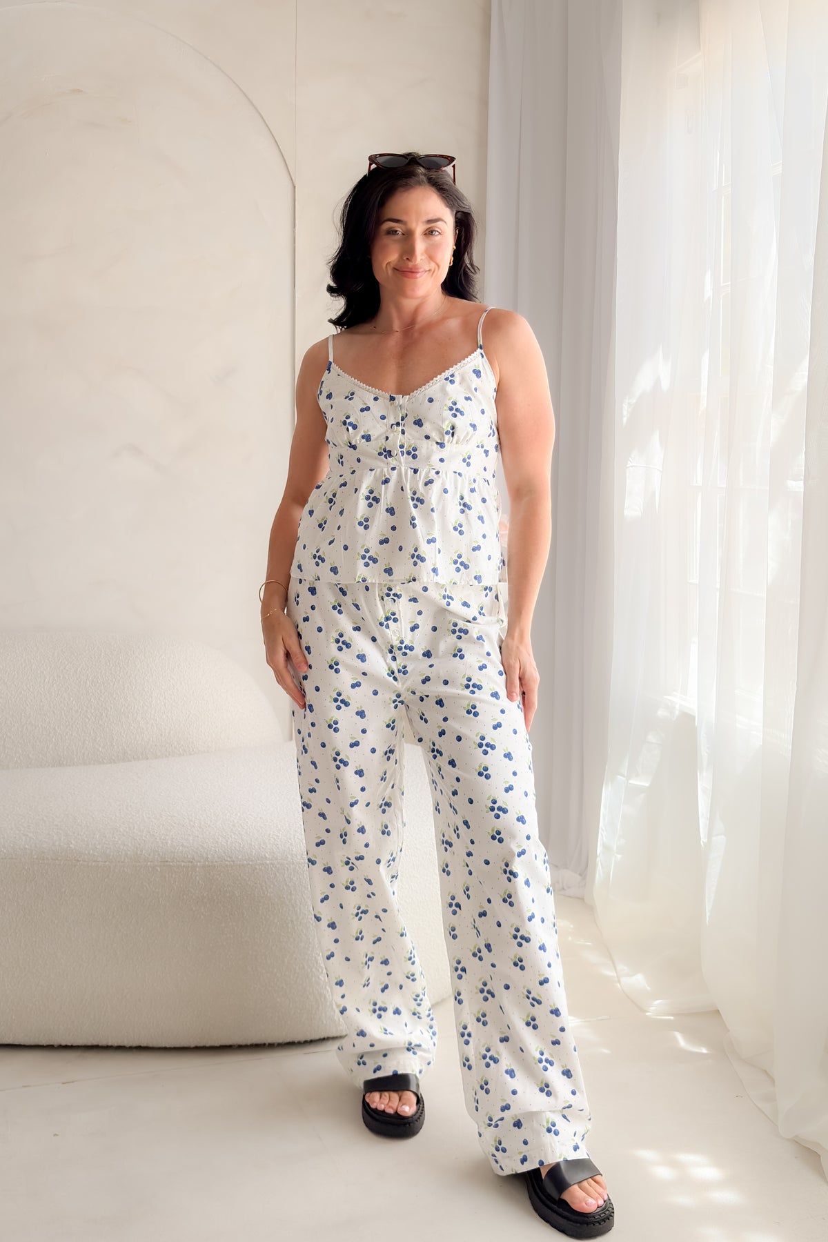 Woman wearing white blueberry print cotton poplin pants with decorative button fly, soft elastic waistband, wide-leg silhouette, and relaxed summer styling.