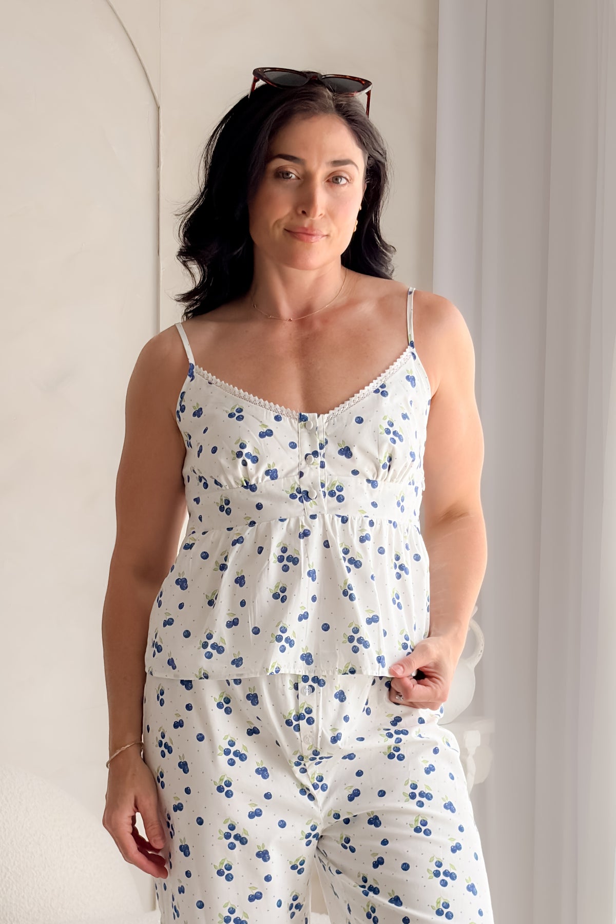 Woman wearing a white blueberry print babydoll tank top with lace trim neckline, adjustable straps, and feminine gathered silhouette.