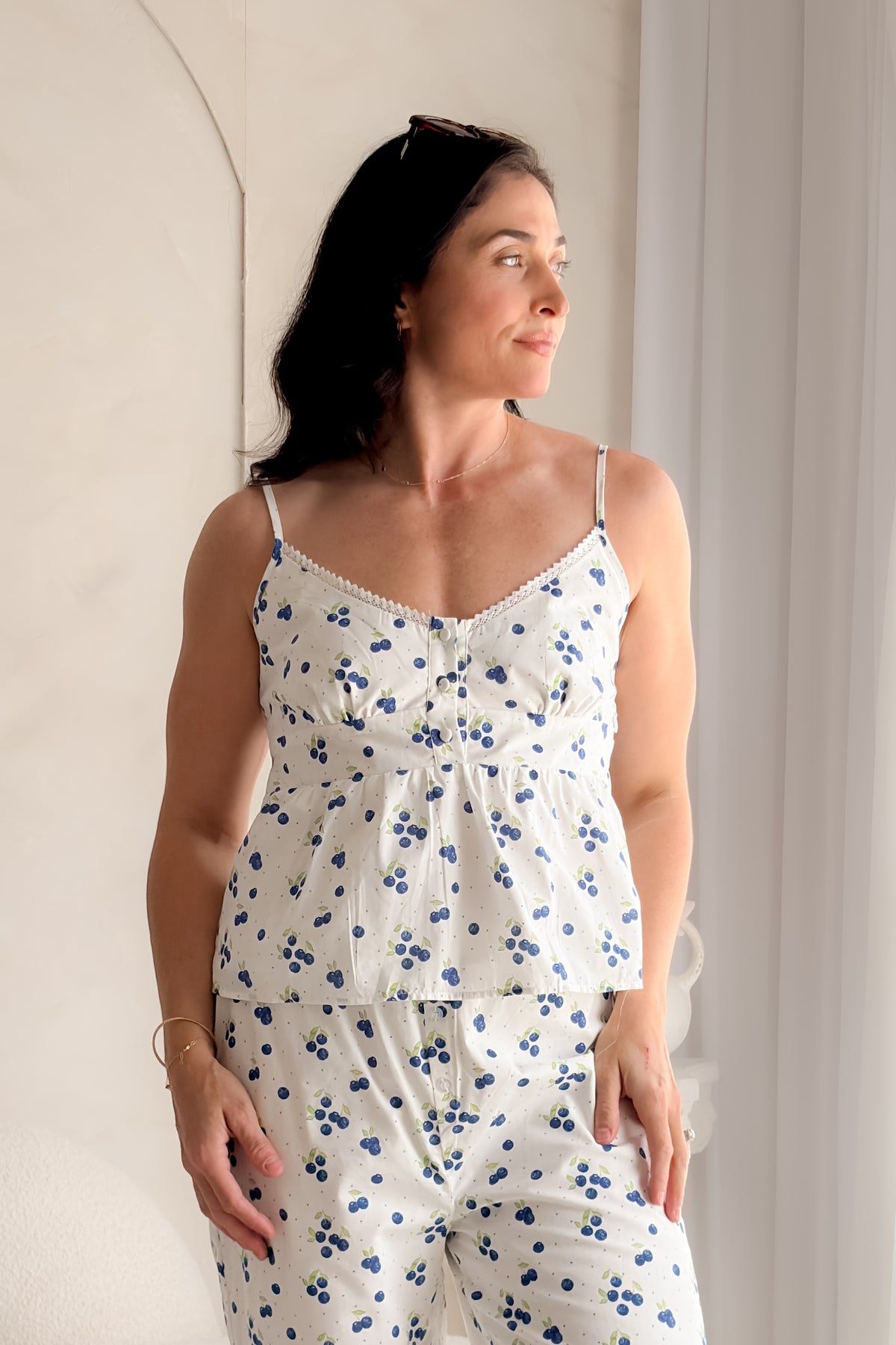 Woman wearing a white blueberry print babydoll tank top with lace trim neckline, adjustable straps, and feminine gathered silhouette.