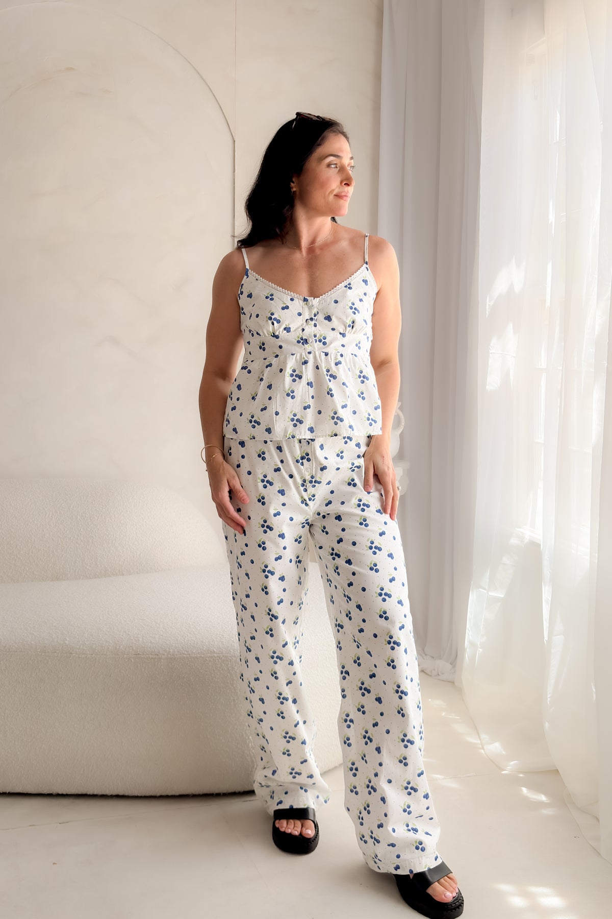 Woman wearing a white blueberry print babydoll tank top with lace trim neckline, adjustable straps, and feminine gathered silhouette.