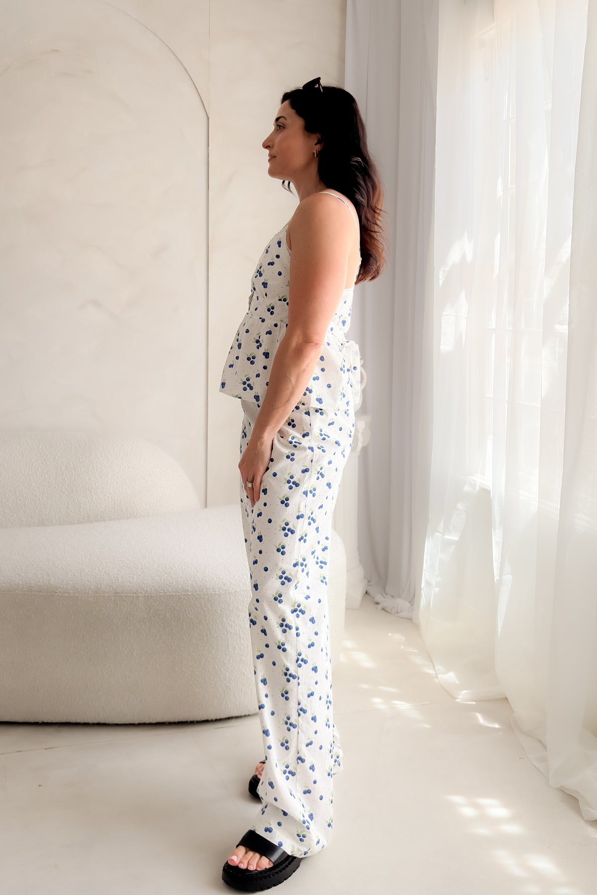 Woman wearing white blueberry print cotton poplin pants with decorative button fly, soft elastic waistband, wide-leg silhouette, and relaxed summer styling.