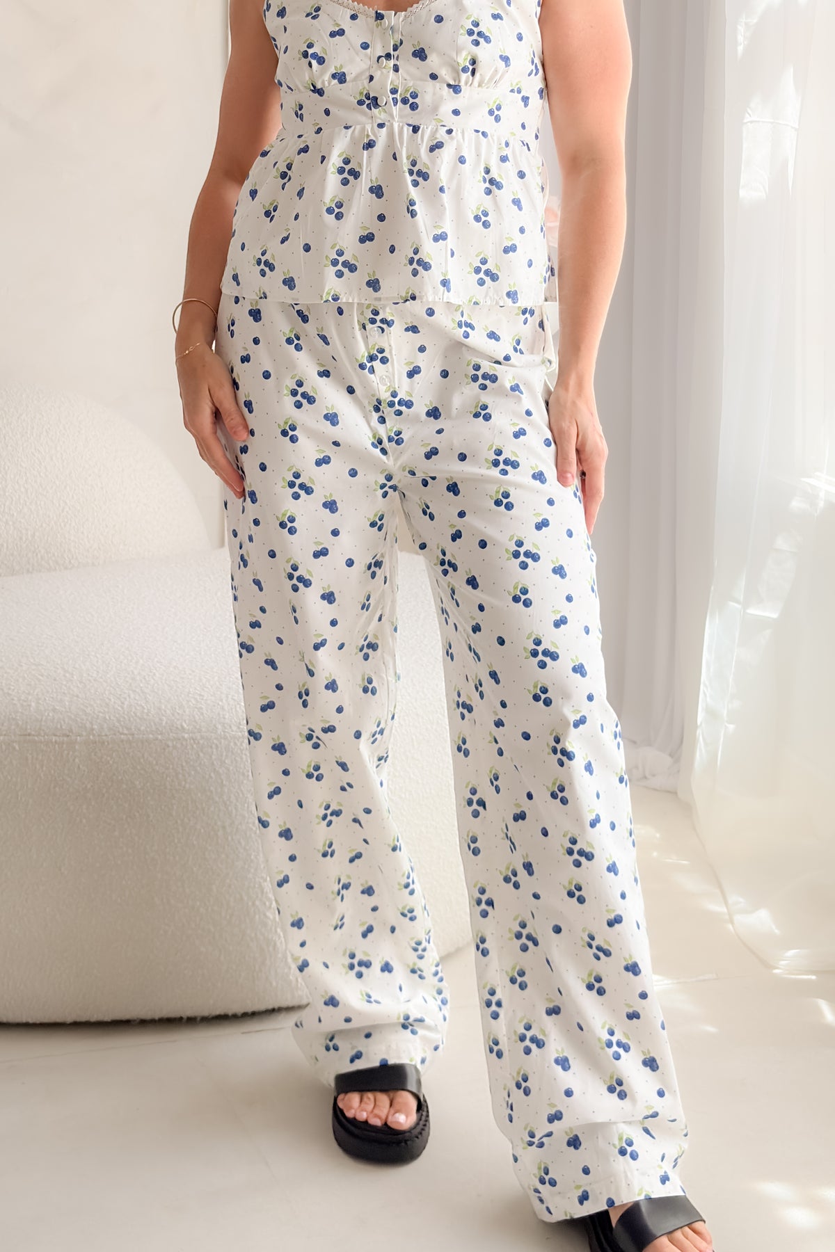 Woman wearing white blueberry print cotton poplin pants with decorative button fly, soft elastic waistband, wide-leg silhouette, and relaxed summer styling.