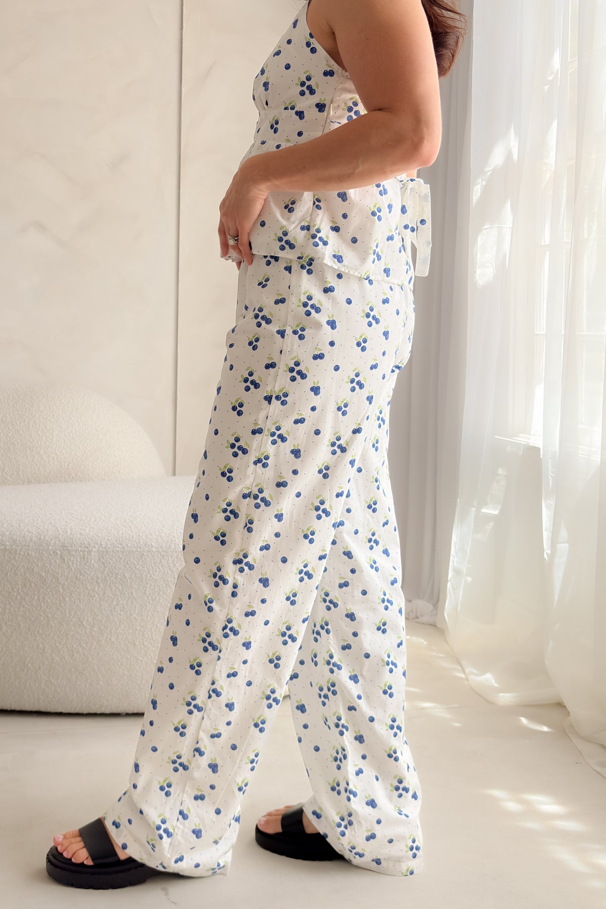 Woman wearing white blueberry print cotton poplin pants with decorative button fly, soft elastic waistband, wide-leg silhouette, and relaxed summer styling.