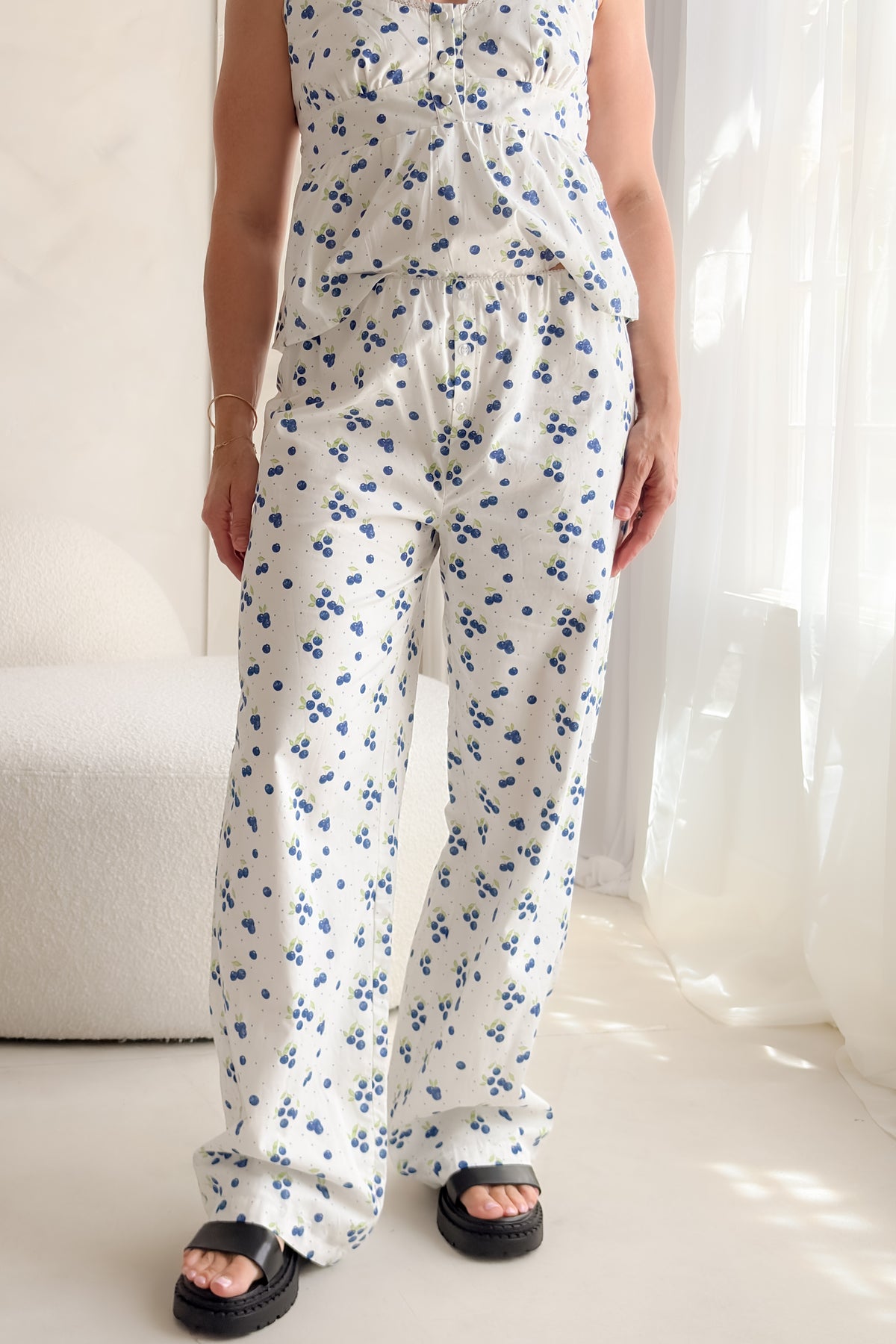 Woman wearing white blueberry print cotton poplin pants with decorative button fly, soft elastic waistband, wide-leg silhouette, and relaxed summer styling.