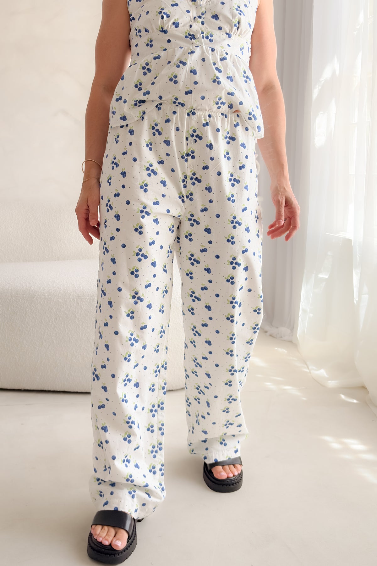 Woman wearing white blueberry print cotton poplin pants with decorative button fly, soft elastic waistband, wide-leg silhouette, and relaxed summer styling.