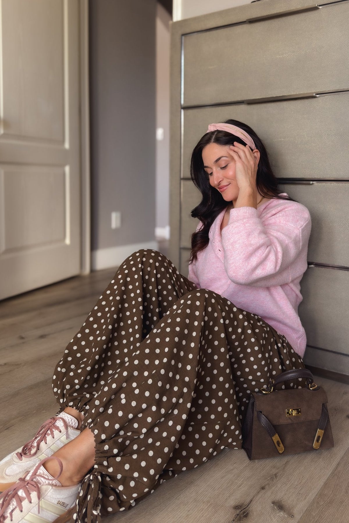 Women’s brown polka dot balloon pants with gathered tie hems paired with a pink button-front cardigan and sneakers.