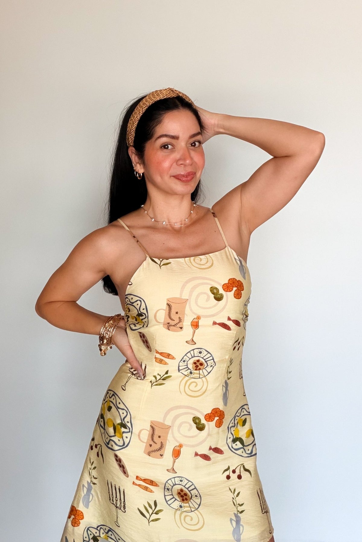 Closer front view of a butter yellow mini dress featuring a colorful Mediterranean food print and slim spaghetti straps.