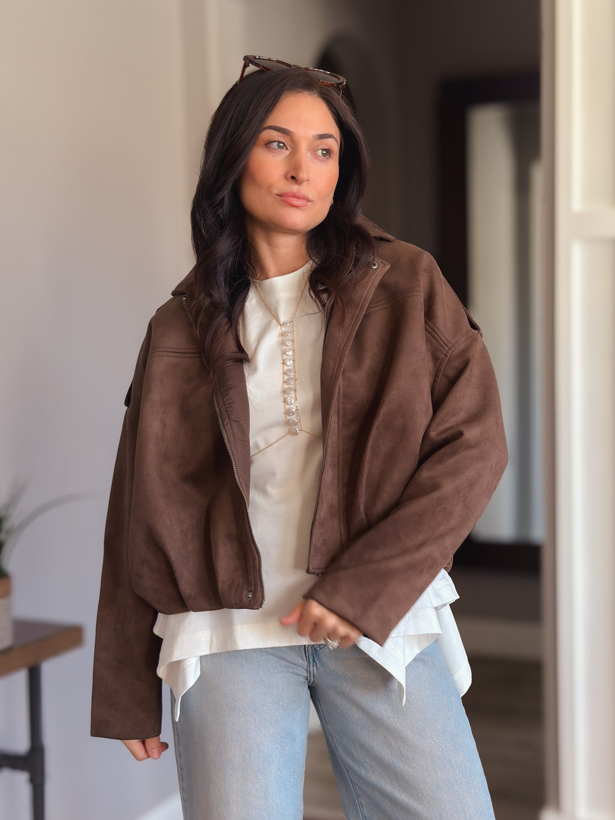 Chocolate brown faux suede jacket shown open over an ivory layered top with light wash jeans.