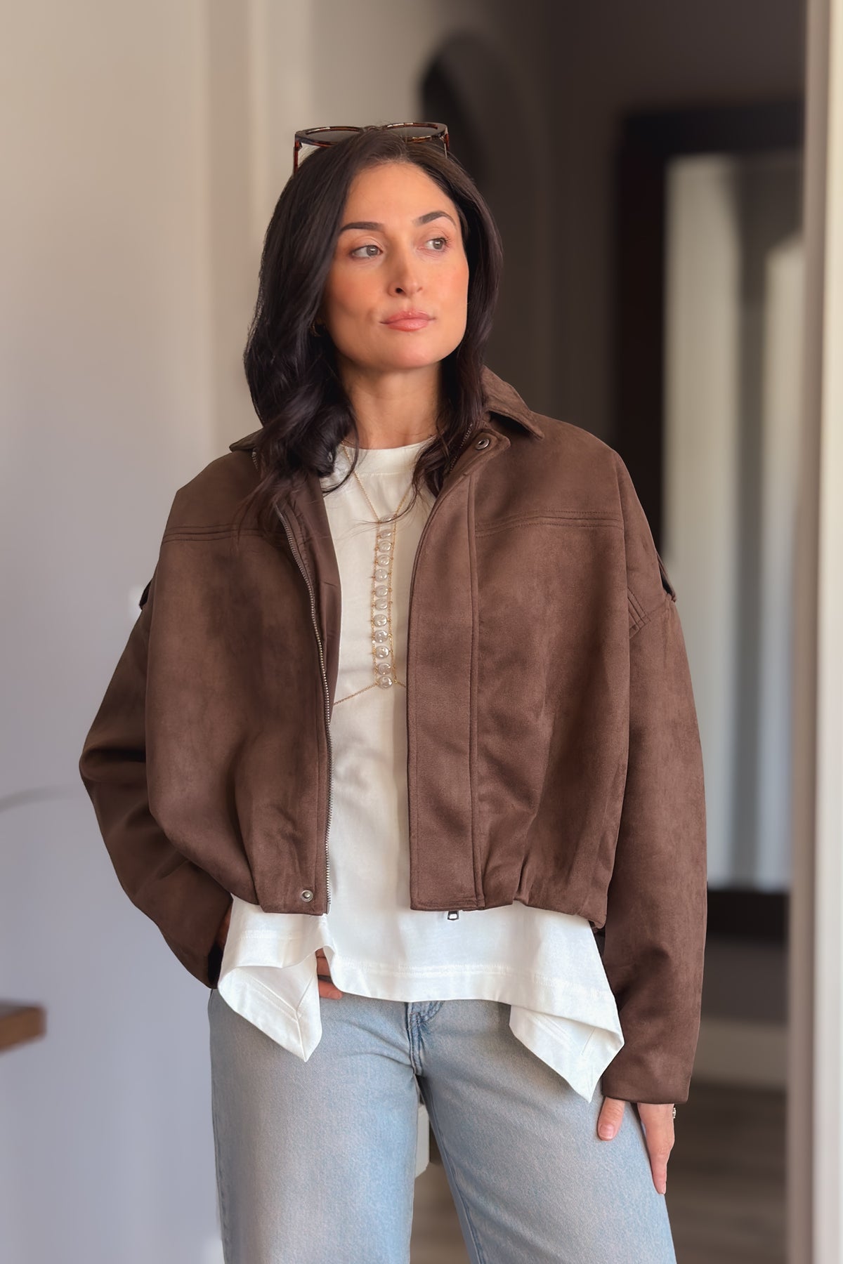 Chocolate brown faux suede bomber jacket with a relaxed boxy fit styled over an ivory top and light wash jeans.