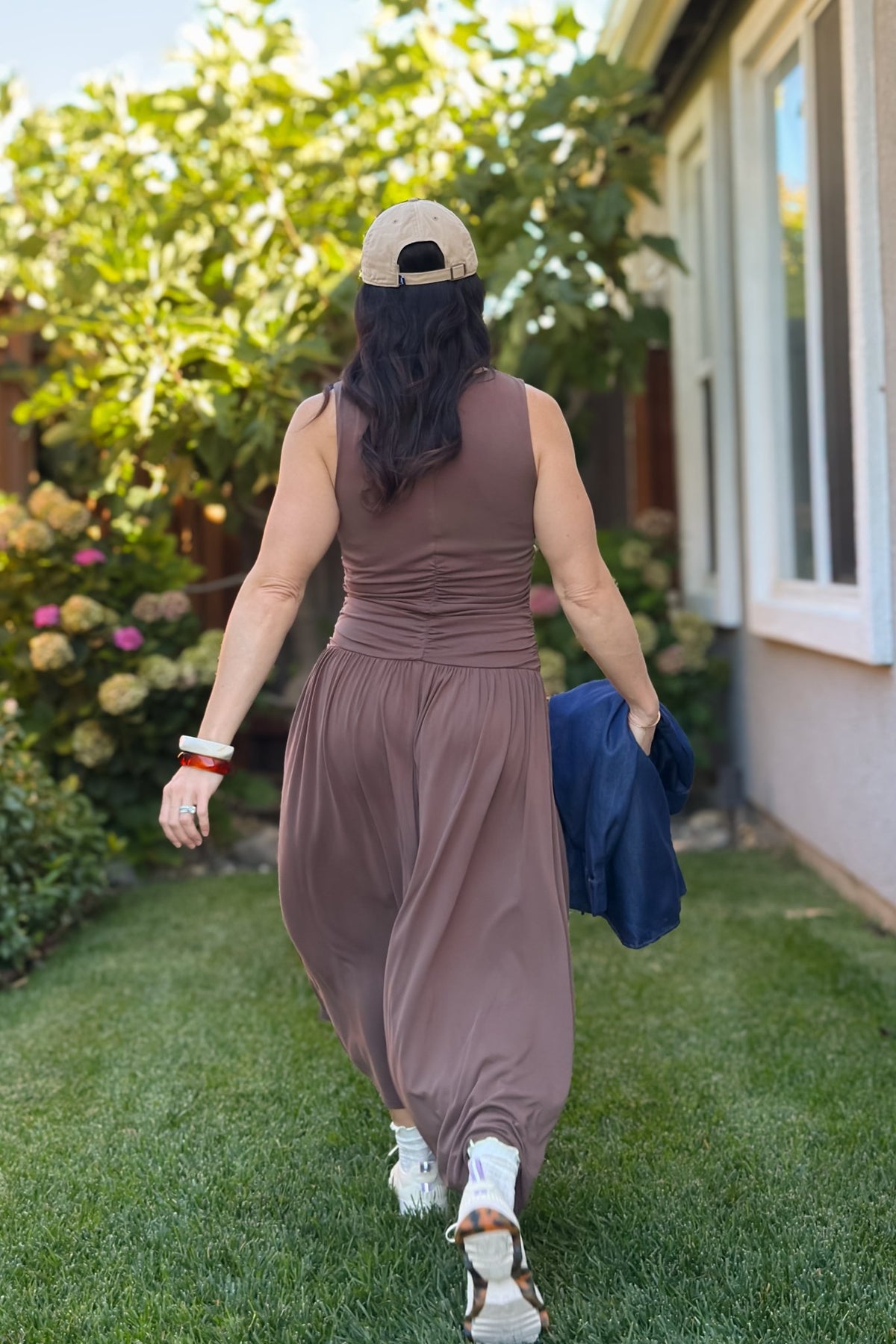 Chocolate brown casual maxi dress styled with a navy denim shirt, neutral sneakers, and a beige baseball cap for transitional weather.