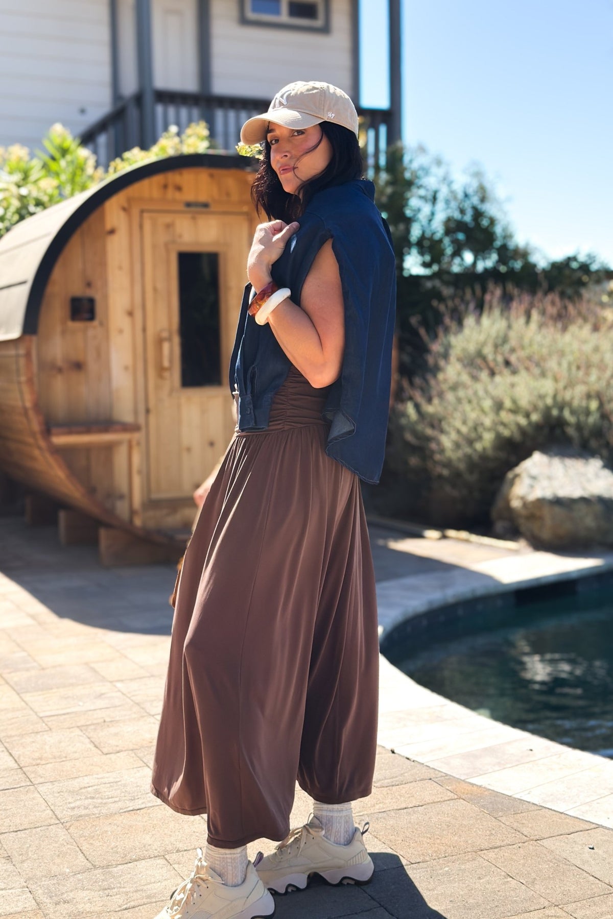 Back view of a chocolate brown sleeveless maxi dress showing the fitted ruched bodice and relaxed flowing skirt.