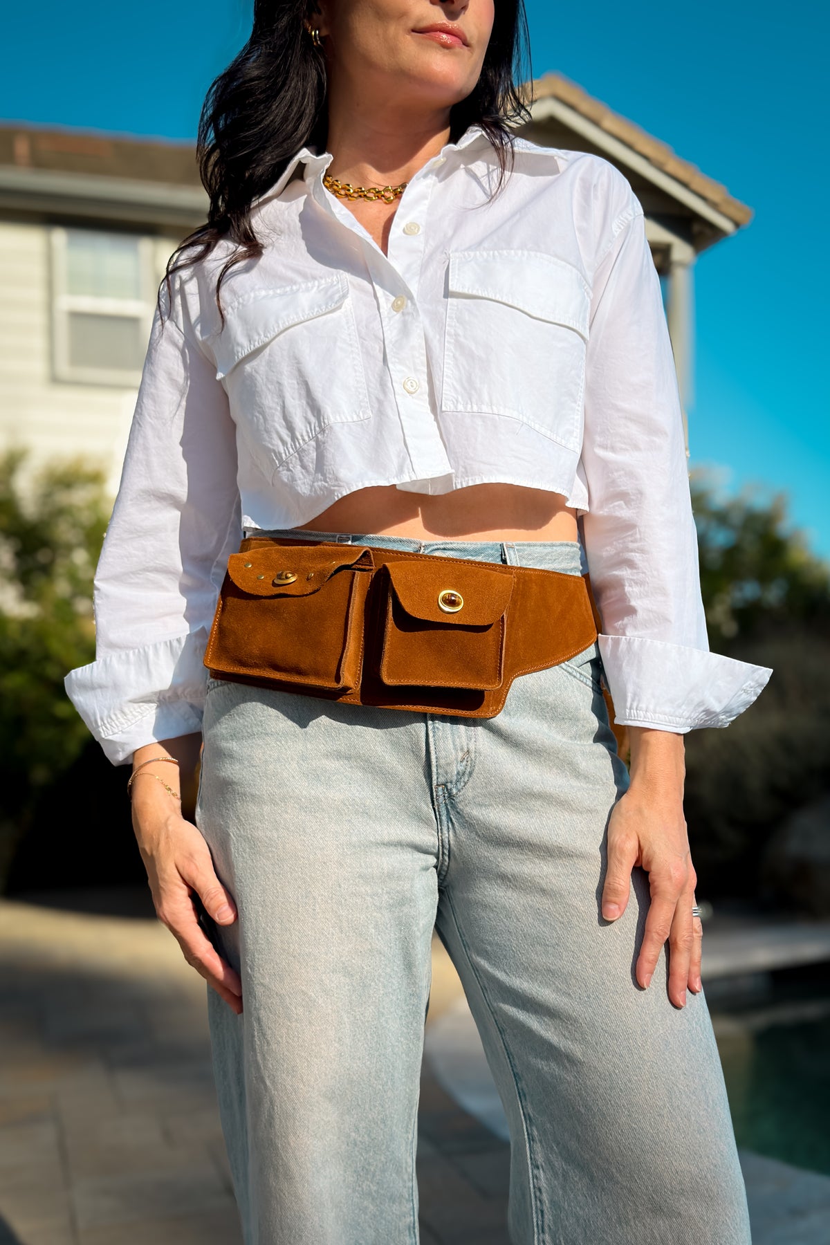 Front view of a cognac suede belt bag featuring two functional pockets, snap closures and a wide adjustable leather strap.