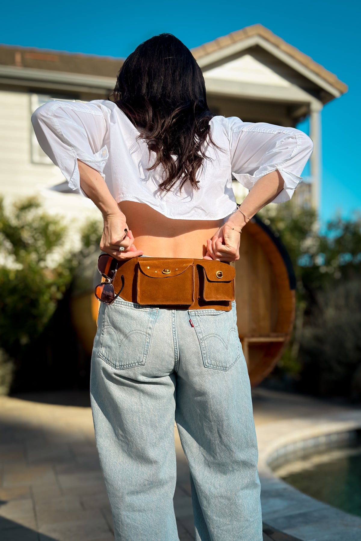 Cognac leather belt bag styled low on the waist with light wash jeans and a white cropped button-down for an easy fall outfit.