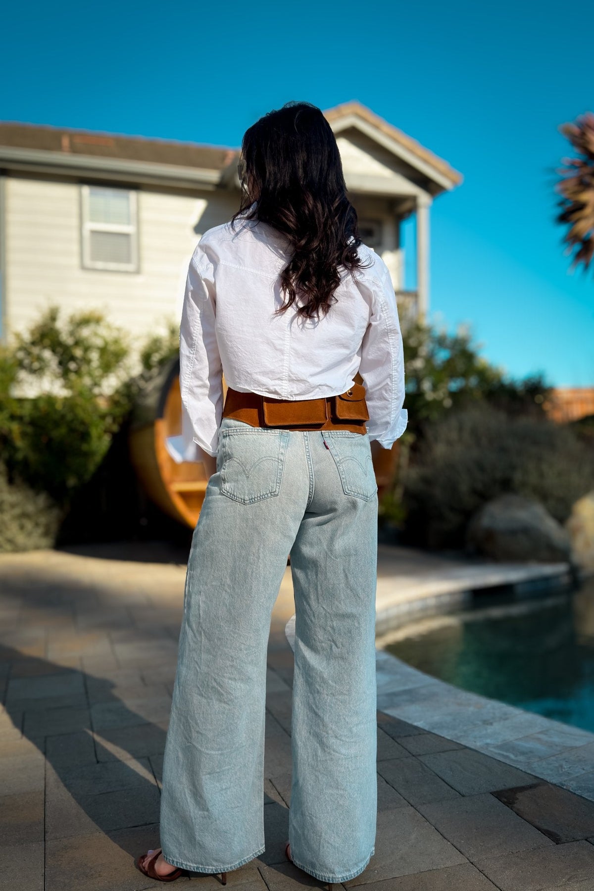 Woman styling a cognac leather belt bag across the waist with relaxed denim and a white shirt for a polished casual look.