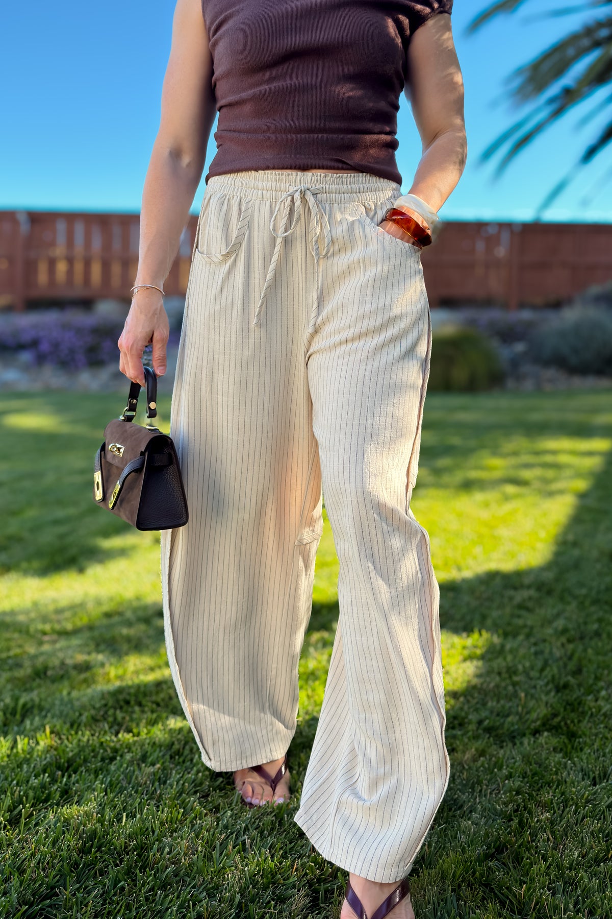 Woman wearing cream striped linen blend wide leg pants with a chocolate brown knit top for an elevated casual outfit.