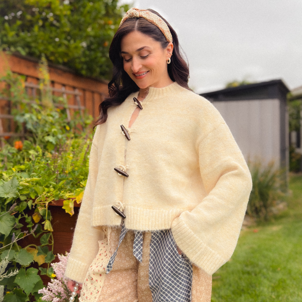 Woman wearing a cream wooden toggle knit cardigan with beige floral patchwork balloon pants for a soft heritage-inspired fall outfit.