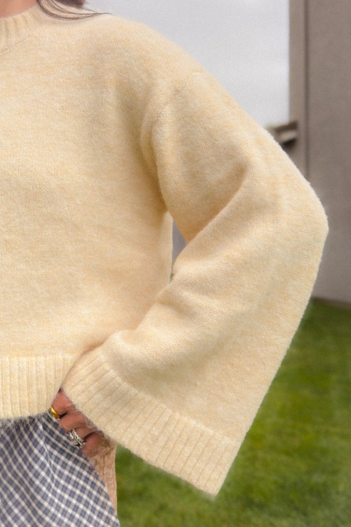 Woman wearing a cream wooden toggle cardigan with oversized sleeves and relaxed fit, paired with beige patchwork balloon pants and a woven handbag.