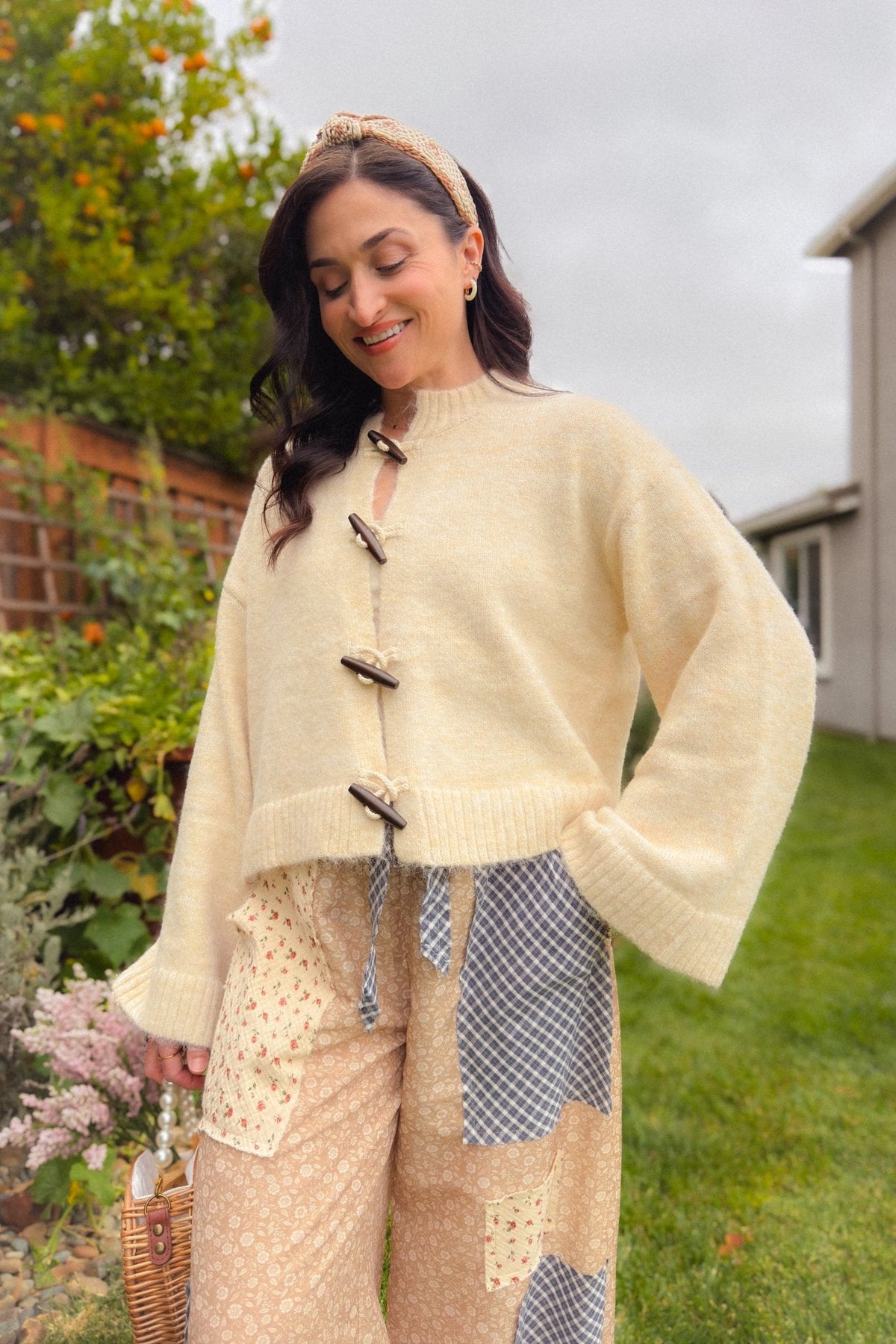 Close-up of cream wooden toggle knit cardigan showing soft textured fabric, relaxed drop shoulder and wide ribbed sleeve.
