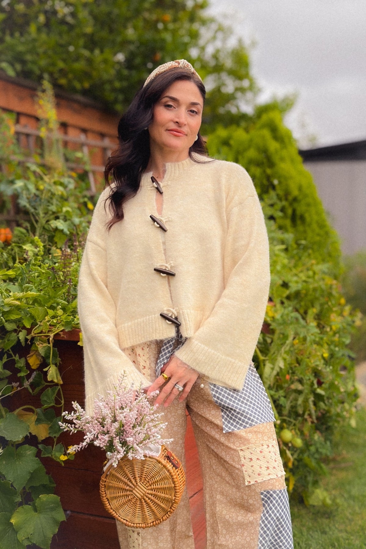 Full-length view of a soft cream knit cardigan with wooden toggle closures, styled with lightweight patchwork balloon pants and woven flats.