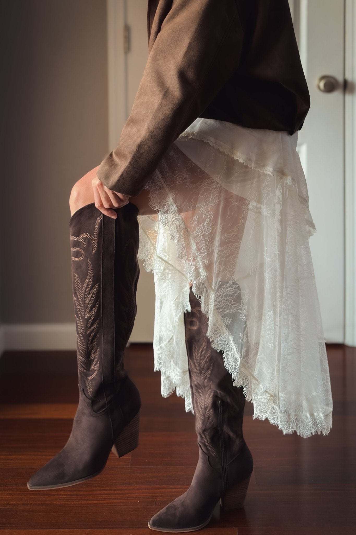 Woman wearing dark brown tall western boots with embroidered shafts, navy plaid shorts and cream cardigan
