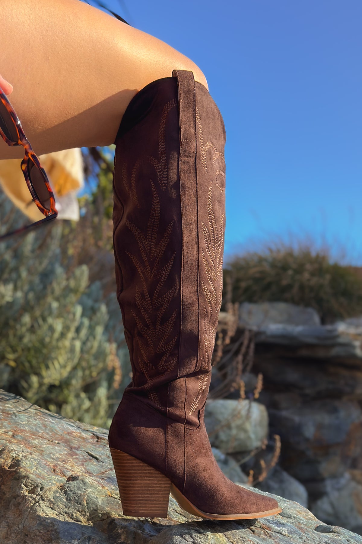 Woman wearing dark brown tall western boots with embroidered shafts, navy plaid shorts and cream cardigan