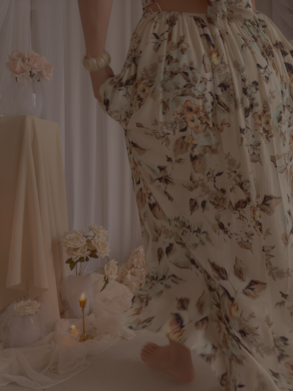 Close-up of a flowy floral summer dress in soft neutral tones with movement, styled in a romantic setting with candles, draped fabric, and delicate florals