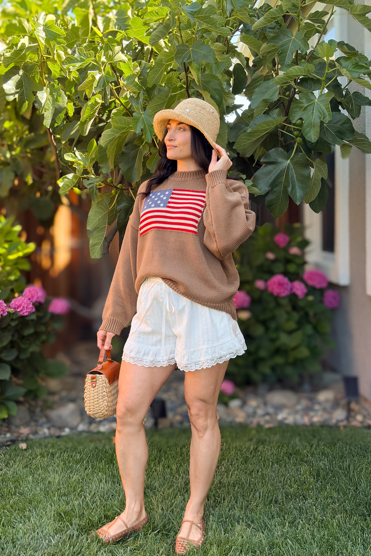Brown heritage American flag sweater paired with ivory lace trim shorts and a straw bucket hat.