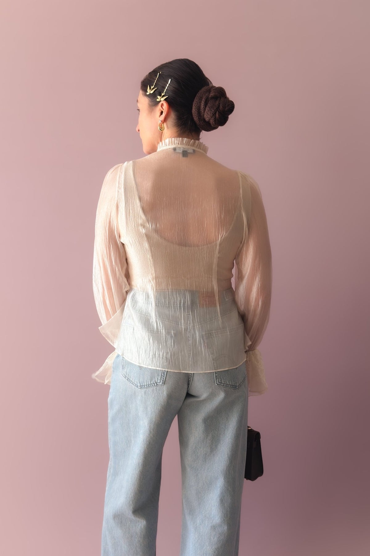 Side view of ivory organza peplum blouse styled with light wash denim and brown handbag
