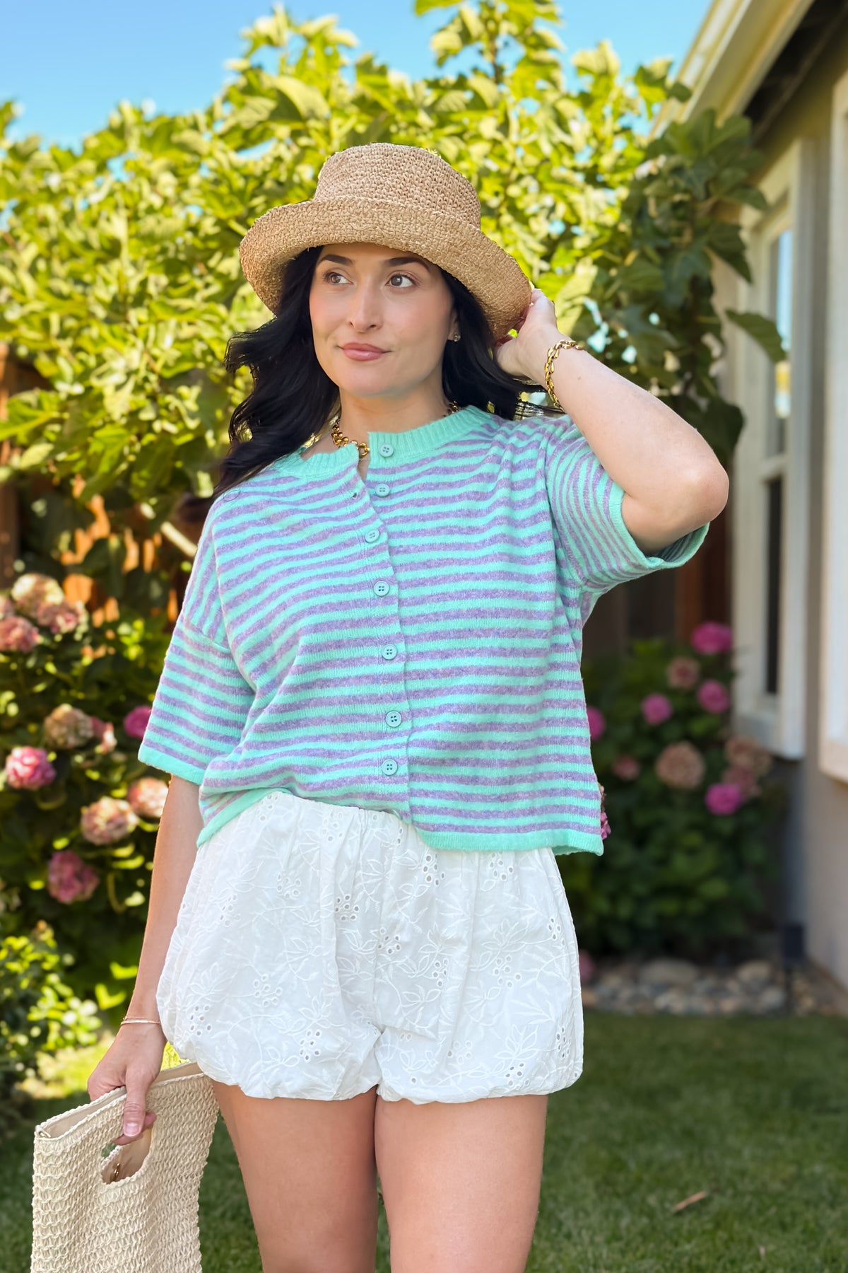 Mint and lavender striped button front sweater styled with eyelet bubble shorts, a woven tote, and straw hat for a coastal summer outfit.