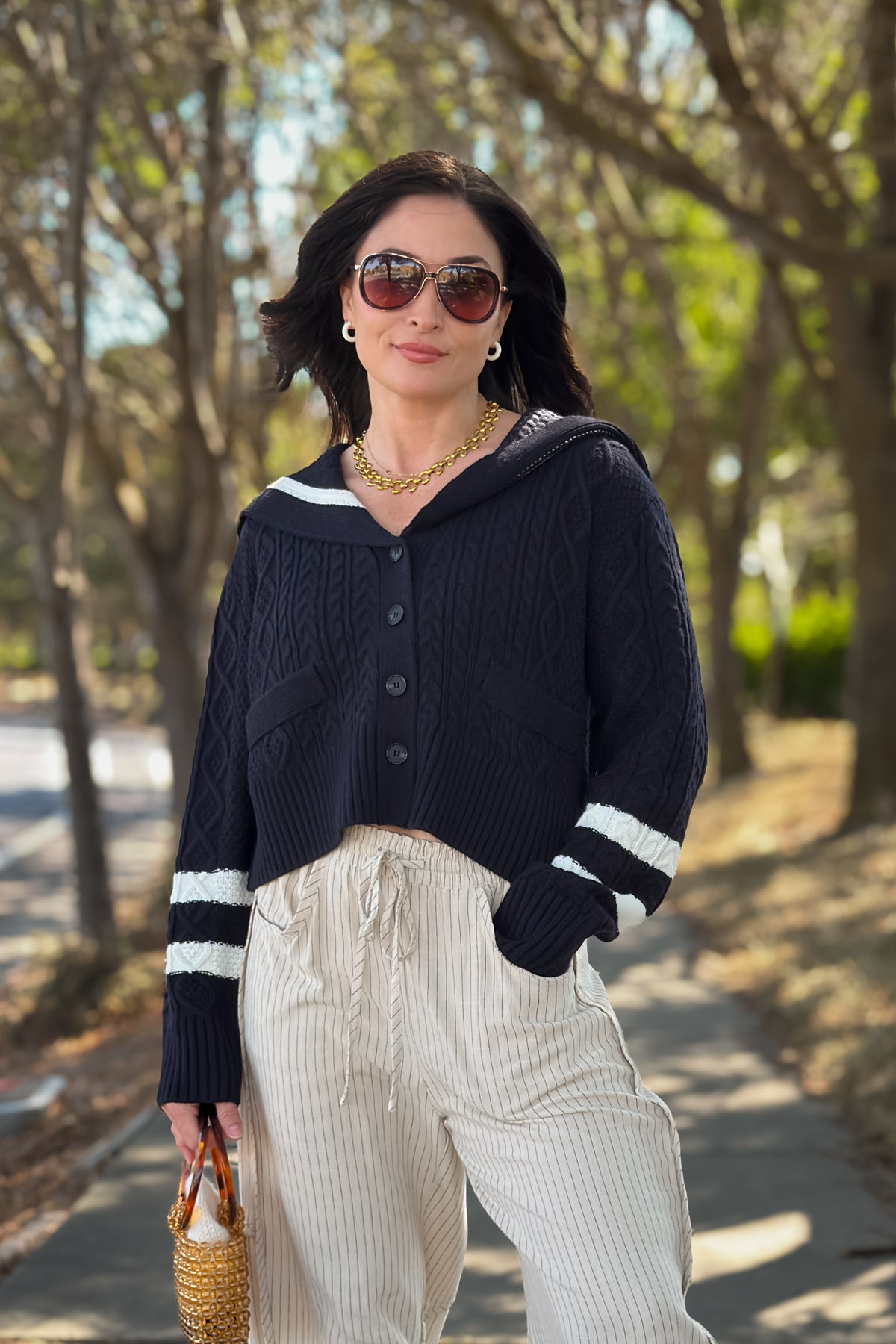 Navy cable knit cardigan sweater with ivory sailor collar and contrast stripe details, styled with cream wide leg pants.