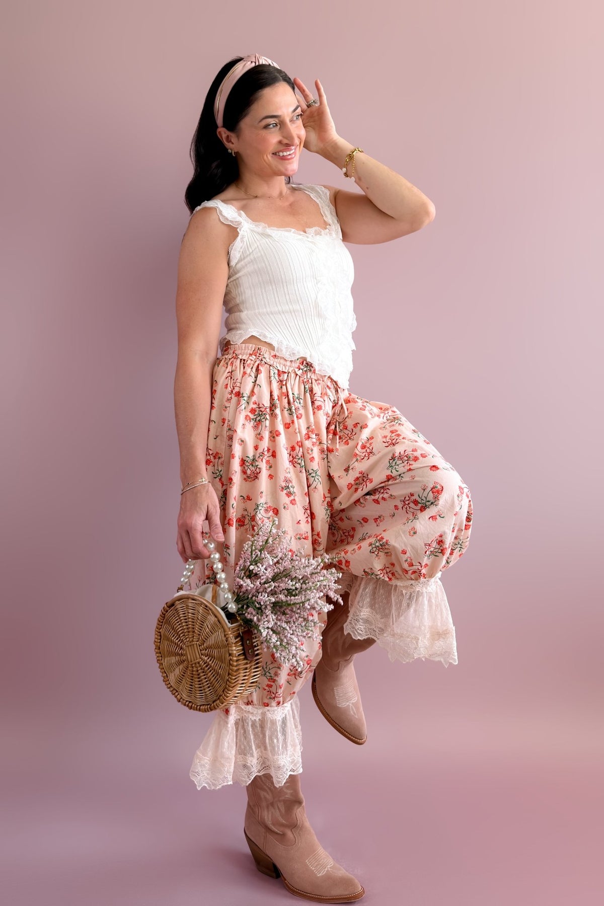 Woman modeling pink floral balloon pants with ivory lace hems, white lace top, western boots, and floral basket