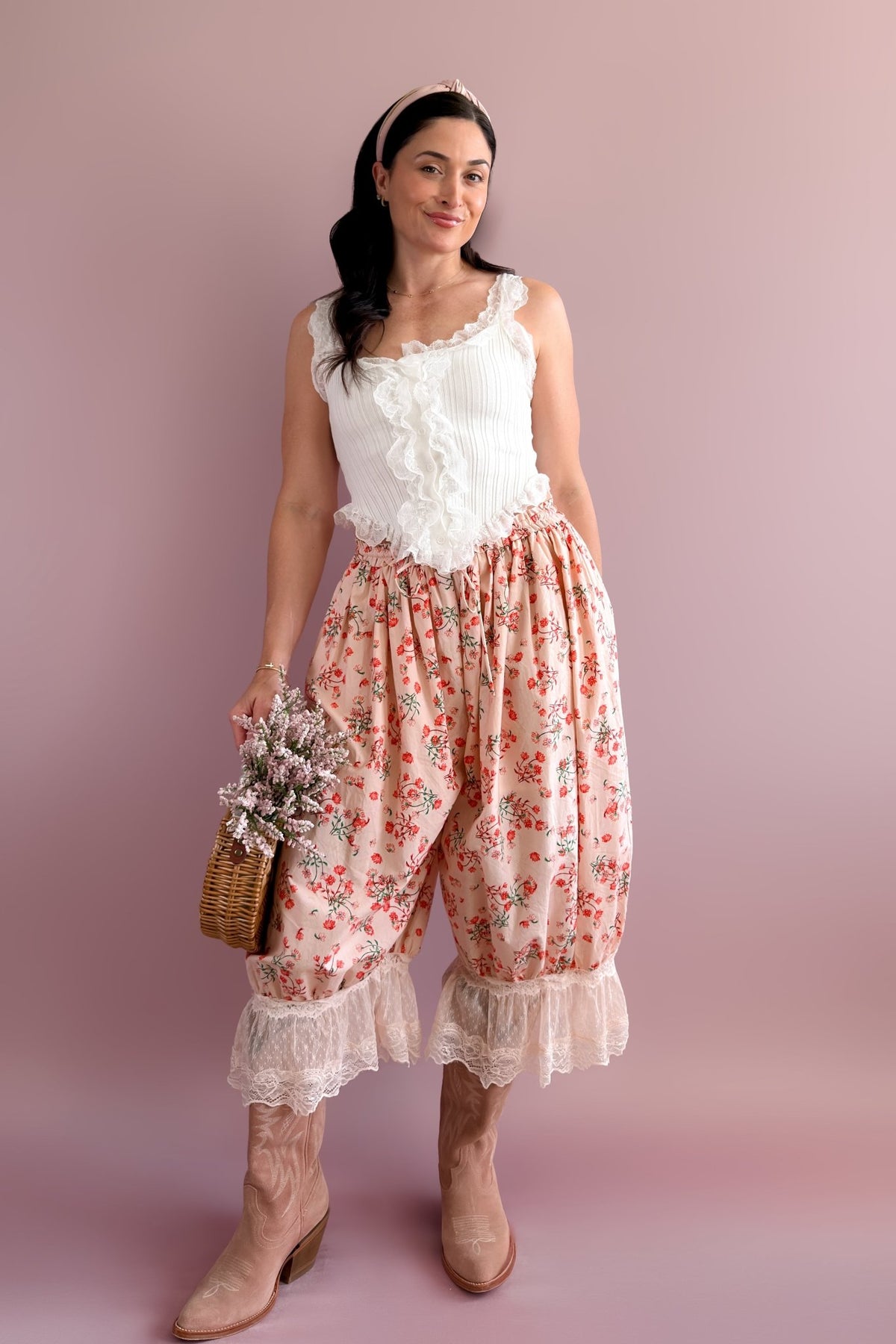 1. Woman modeling pink floral balloon pants with ivory lace hems, white lace top, western boots, and floral basket