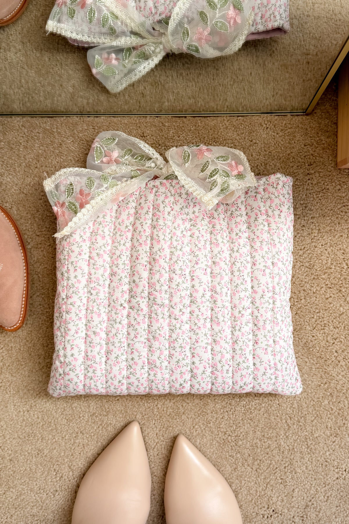 Pink floral Bible study cover with delicate green and pink embroidered bow displayed beside neutral shoes and books