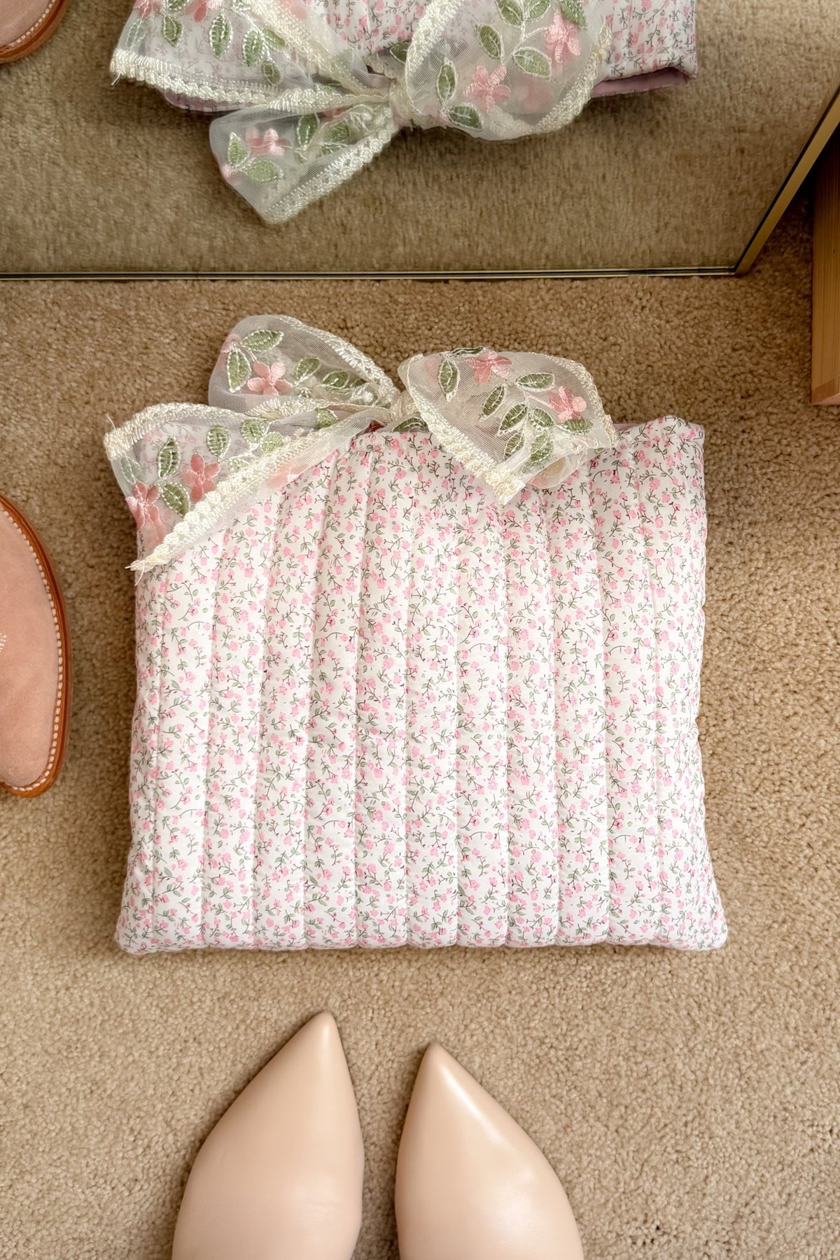 Pink floral Bible study cover with delicate green and pink embroidered bow displayed beside neutral shoes and books