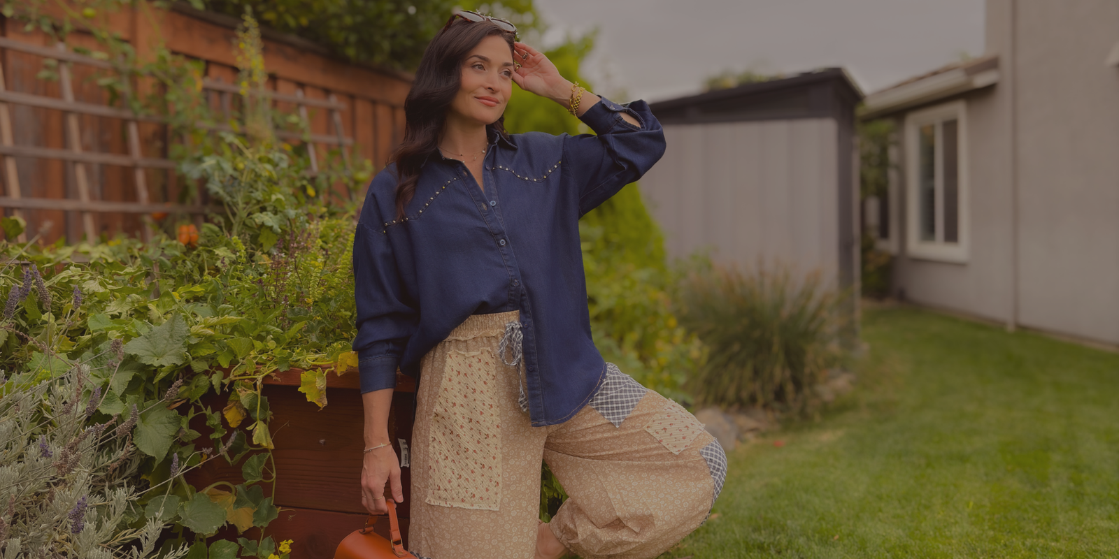 Woman wearing a navy studded denim shirt with beige floral patchwork balloon pants and a woven handbag, styled for Blooming Daily’s Soft Heritage Romance fall collection.