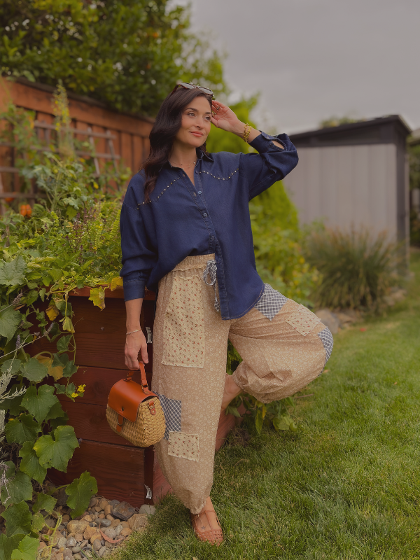 Woman styling a navy denim button-down with beige floral patchwork balloon pants, woven handbag and tan flats for a feminine transitional fall outfit.