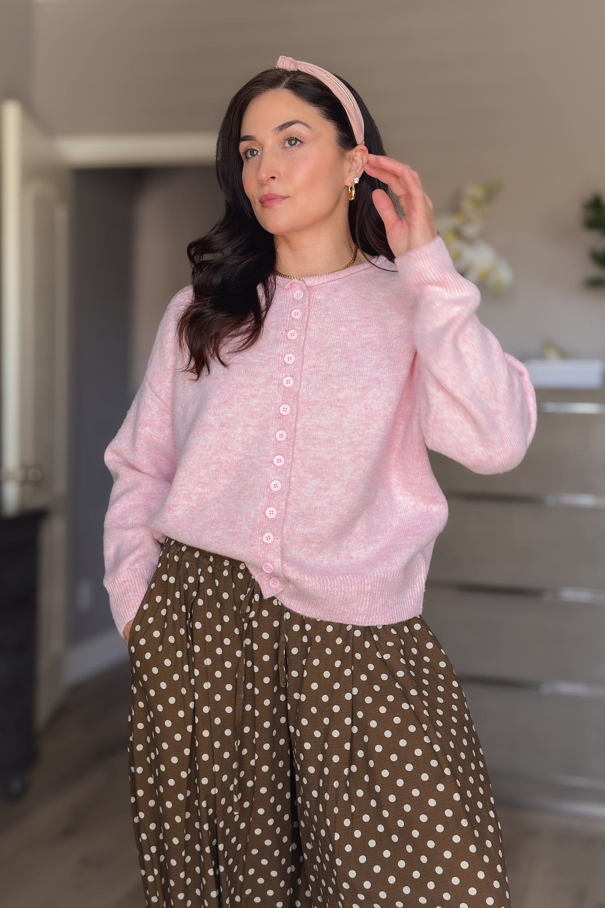 Light pink button front cardigan sweater for women styled with brown polka dot pants and a pink headband.