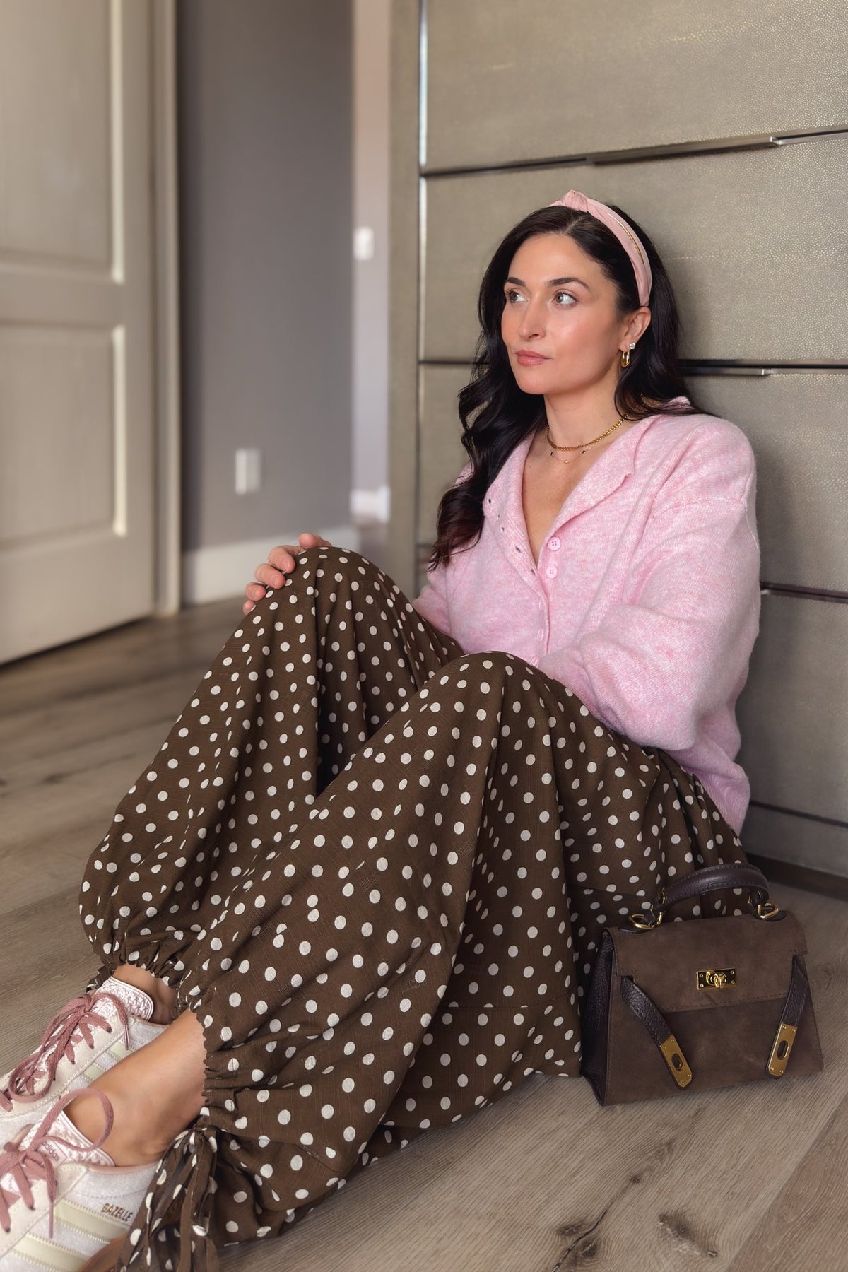 Brown polka dot balloon pants styled with a soft pink cardigan and blush sneakers for a feminine casual outfit.