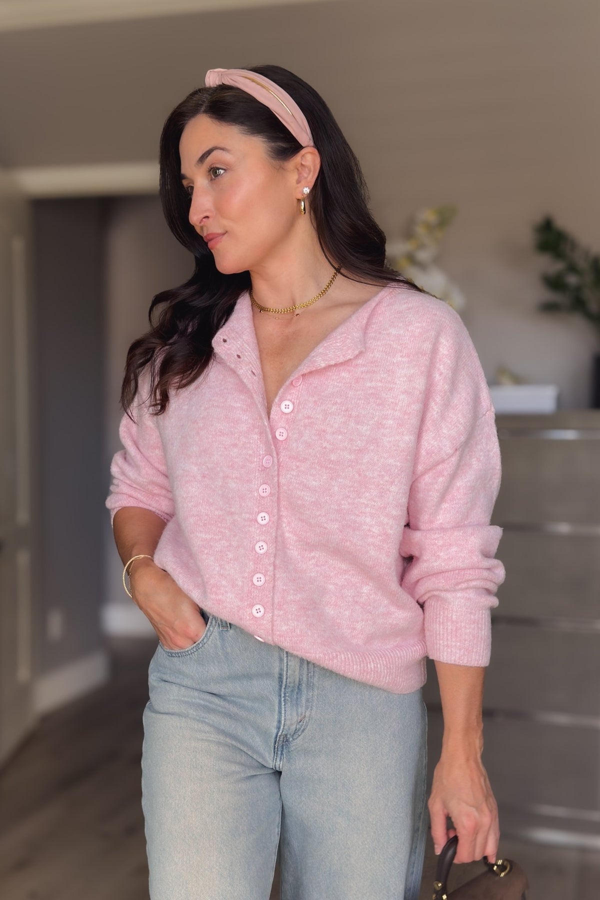 Close-up of soft pink cardigan sweater showing the heathered knit texture, ribbed hem, and matching pink buttons.