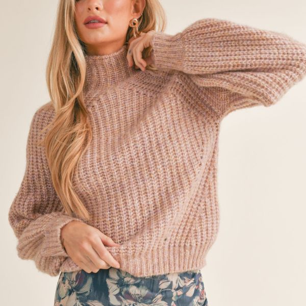 A blonde model wearing a blush colored sweater and posing elegantly
