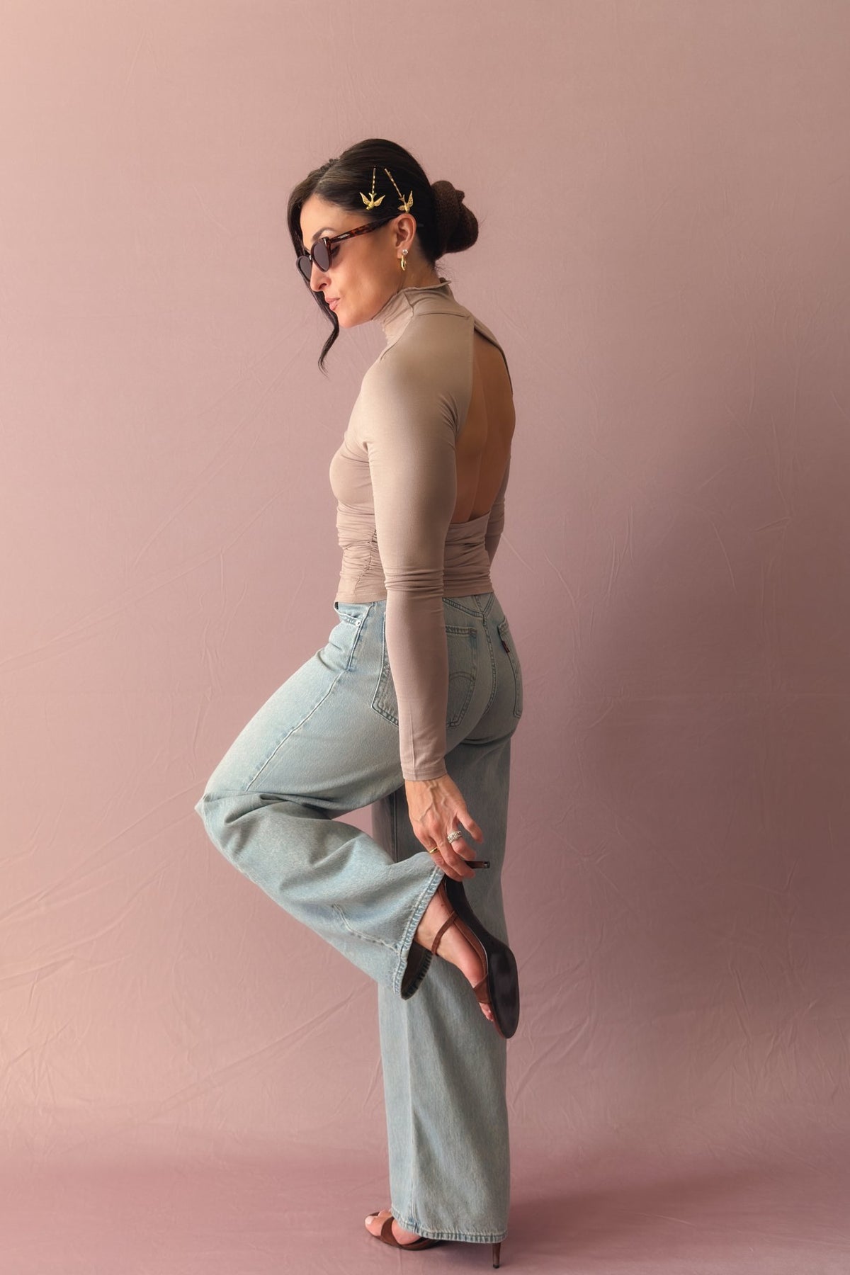 Taupe open back turtleneck top with fitted long sleeves and light wash jeans