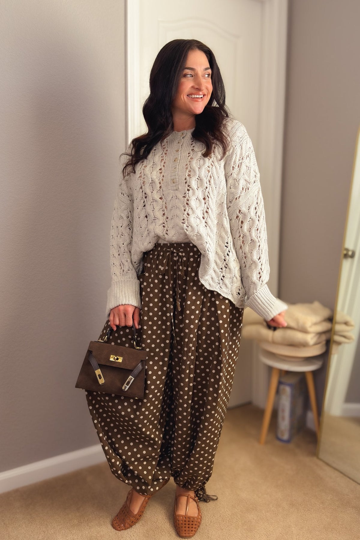 Women’s brown polka dot balloon pants paired with an ivory open-knit sweater and structured brown handbag.