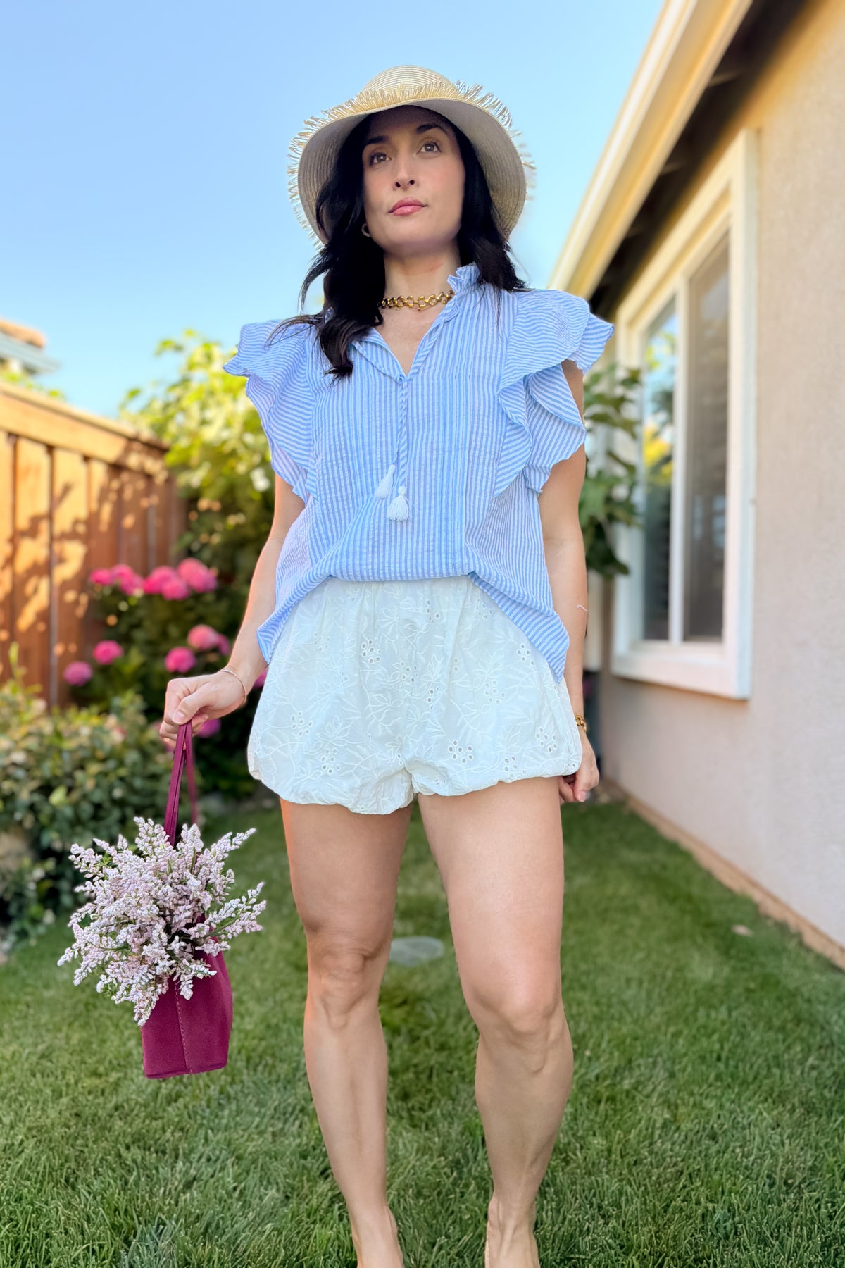Women's white eyelet bubble shorts styled for summer with a lightweight striped cotton blouse and straw hat.