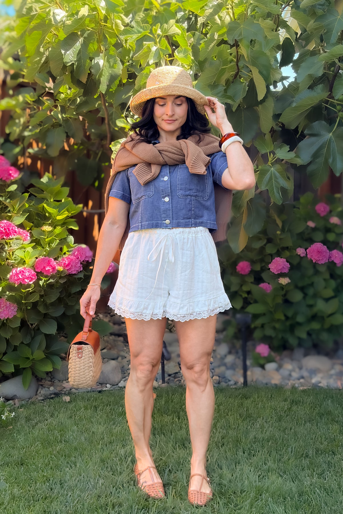 Women's white lace trim shorts paired with a cropped denim top and lightweight sweater for a casual summer outfit.